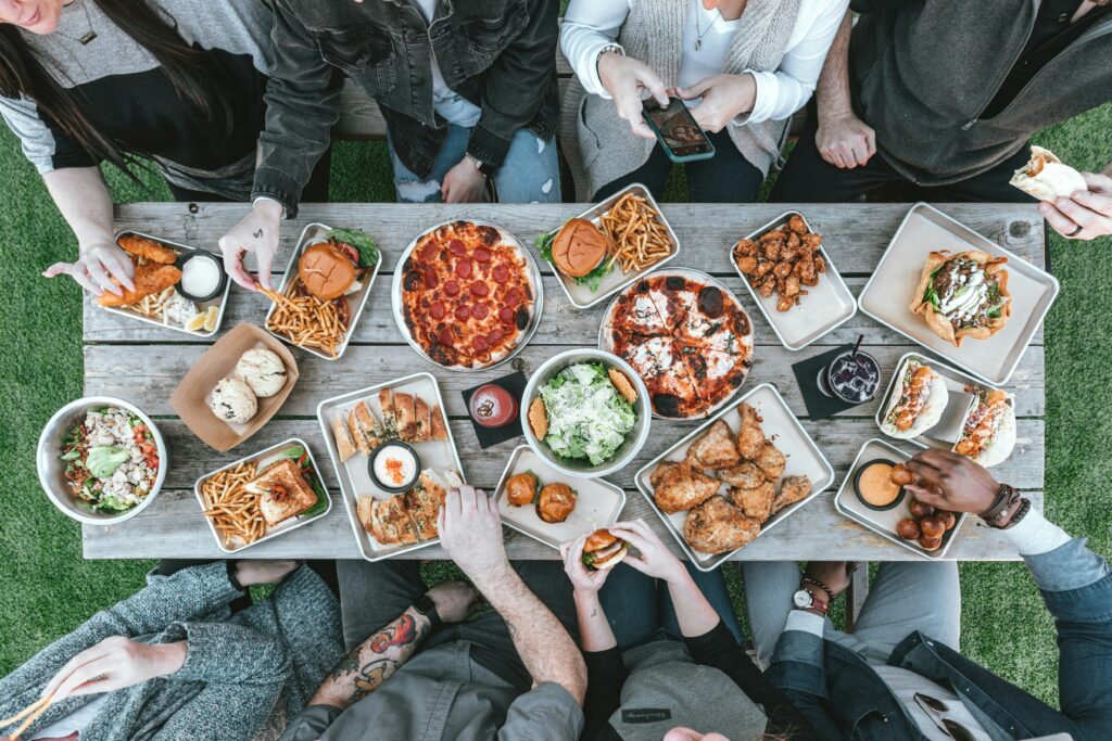 芝生の上で、パンやピザ、ポテトなど食事を囲む様子。